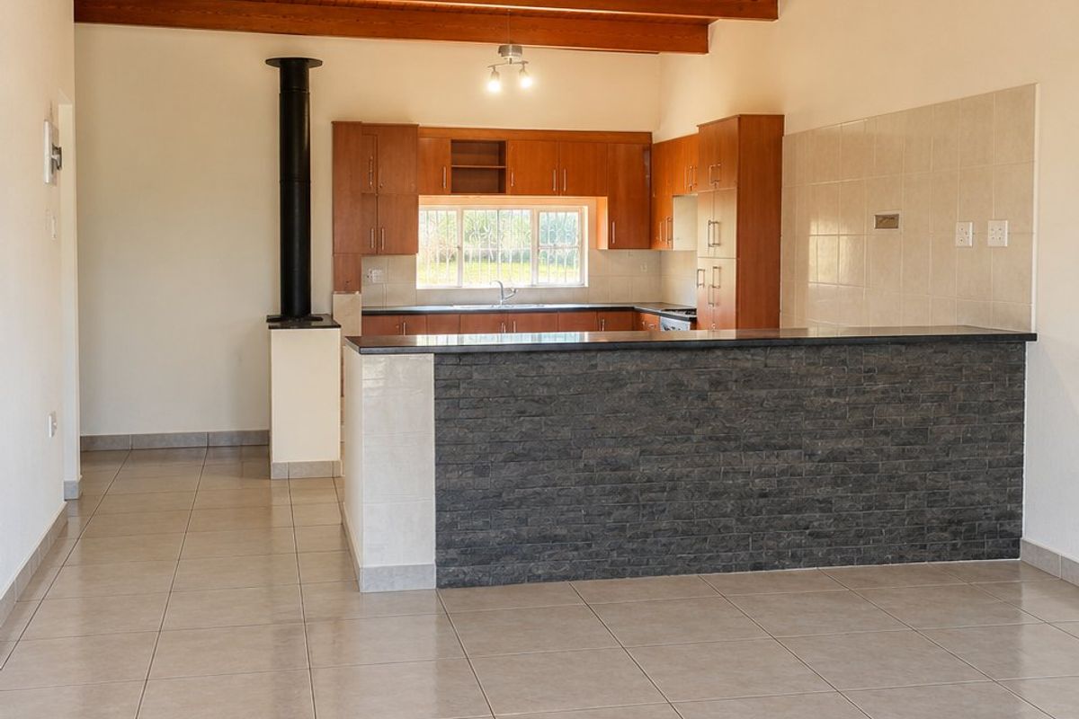 Spacious open-plan living and kitchen area featuring exposed timber ceiling beams, tiled flooring, a stone-clad breakfast bar, and a built-in fireplace.