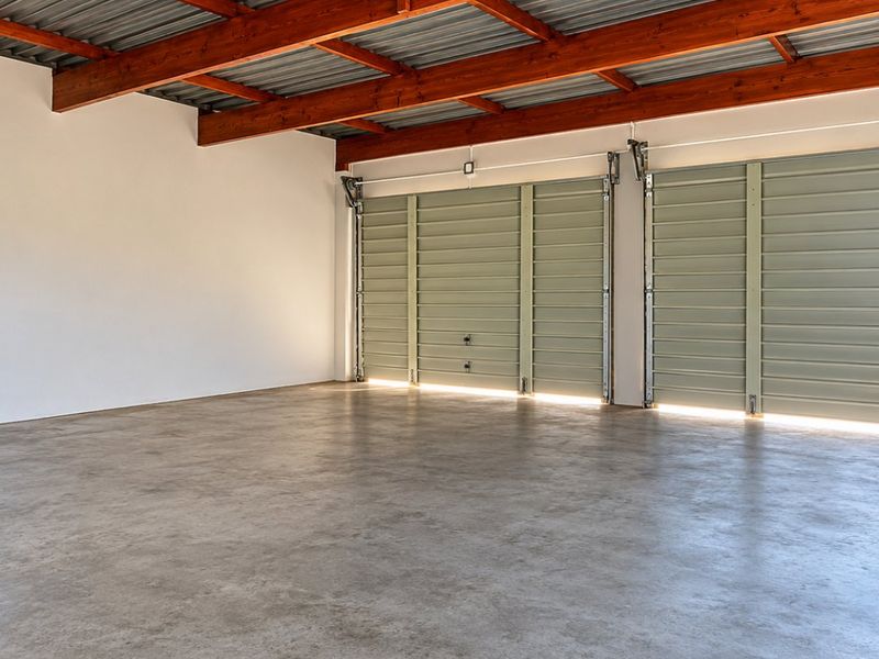 Spacious, well-maintained garage featuring exposed timber beams, a corrugated metal ceiling, and smooth concrete flooring with dual sectional garage doors.