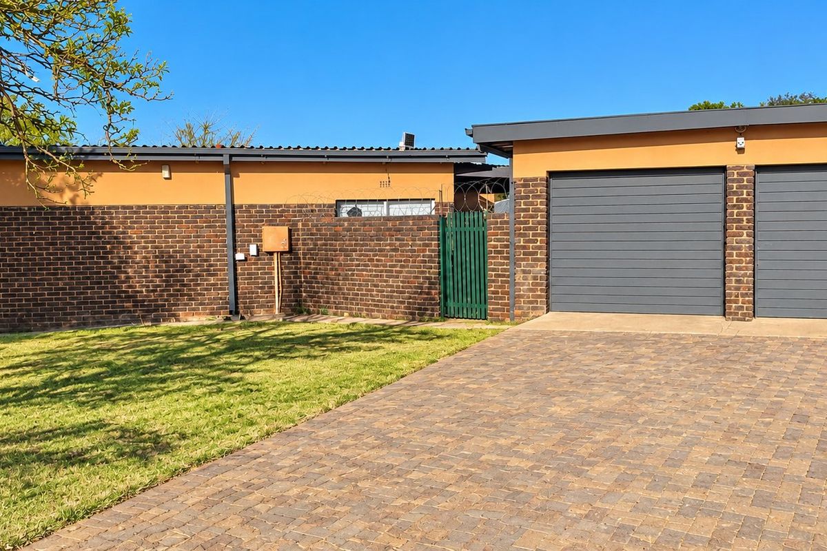 Front view of the property featuring a double garage, paved driveway, and well-maintained brick facade with secure perimeter fencing.