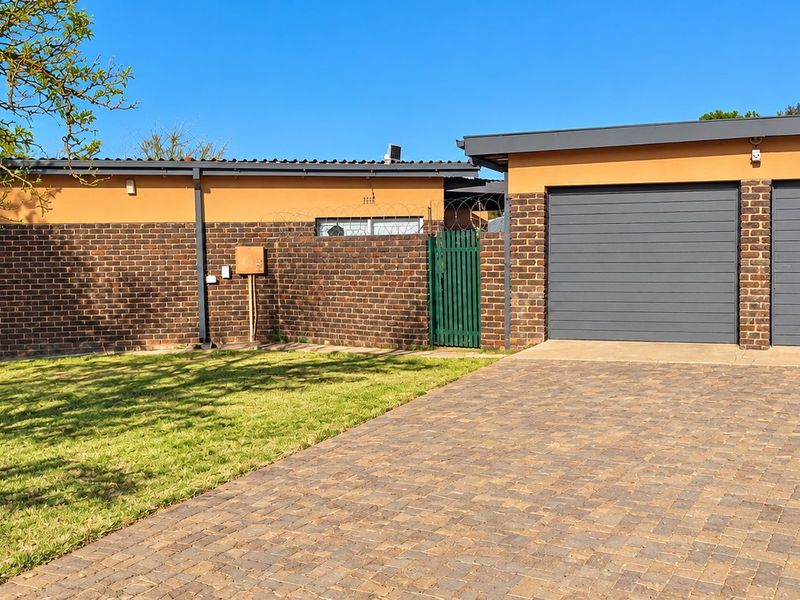 Front view of the property featuring a double garage, paved driveway, and well-maintained brick facade with secure perimeter fencing.