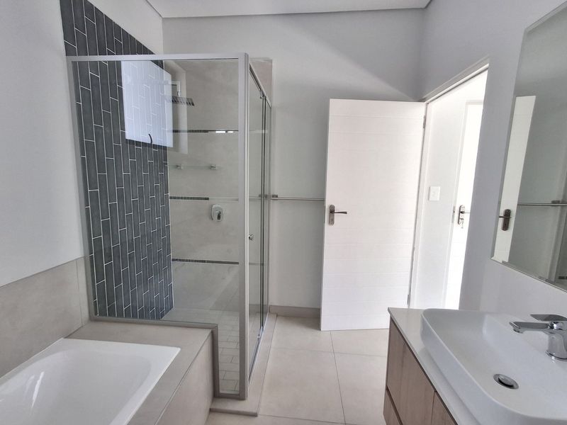 Modern bathroom featuring a glass-enclosed shower, built-in bathtub, and a sleek vanity with a vessel sink, finished with contemporary tiling.