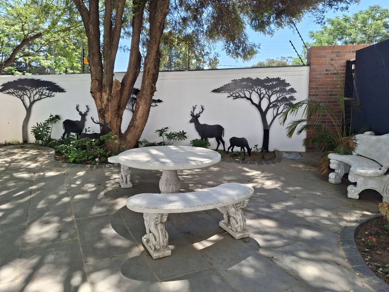 A landscaped garden area featuring stone paving, a boundary wall with decorative metal silhouettes, and established trees.