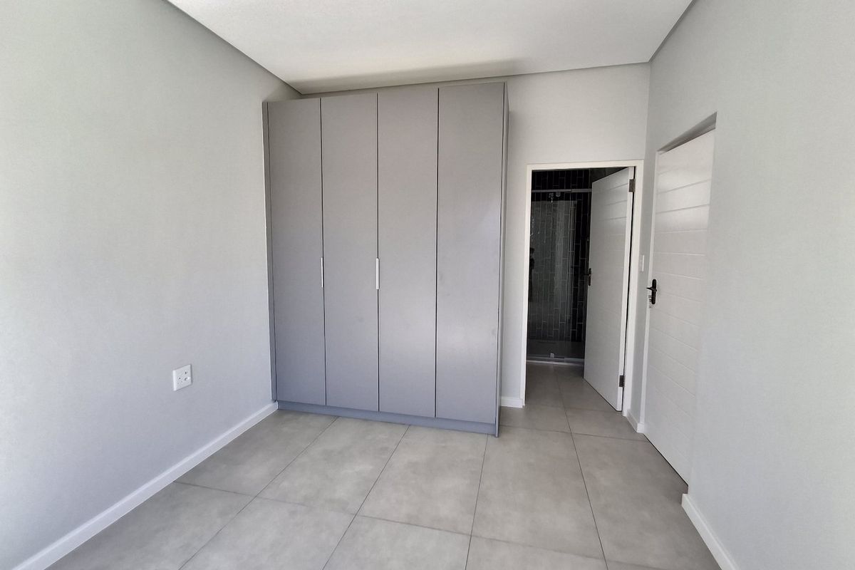A clean, modern bedroom featuring neutral grey tiled flooring, built-in wardrobes, and direct access to an en-suite bathroom.