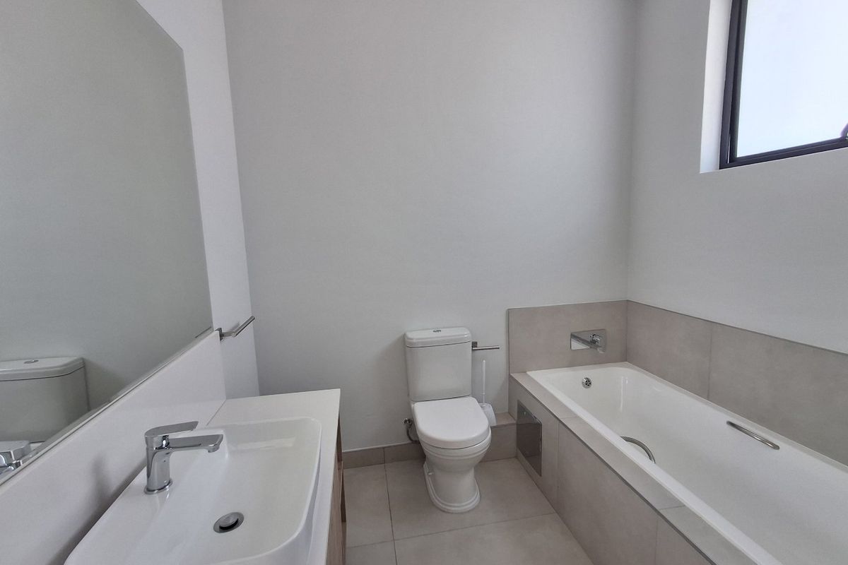 A clean, modern bathroom featuring a built-in vanity, ceramic basin, toilet, and a bathtub with neutral tiling.
