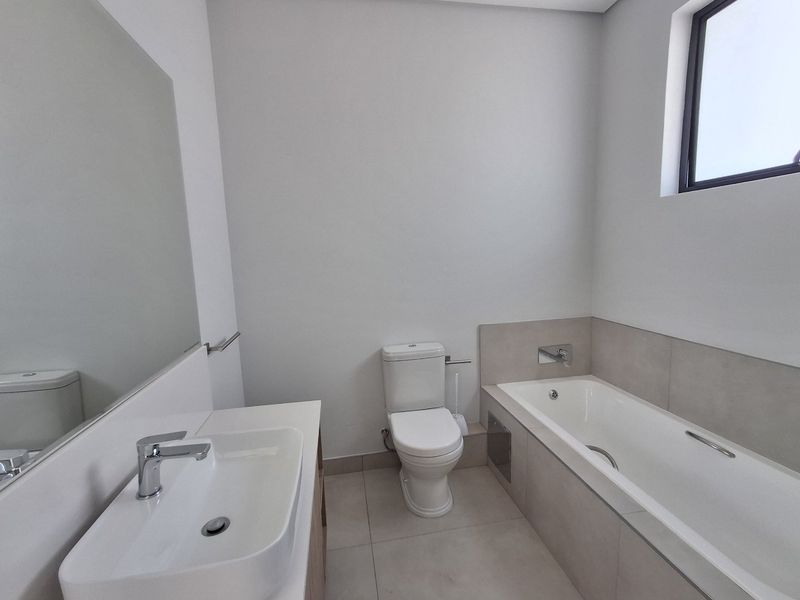 A clean, modern bathroom featuring a built-in vanity, ceramic basin, toilet, and a bathtub with neutral tiling.