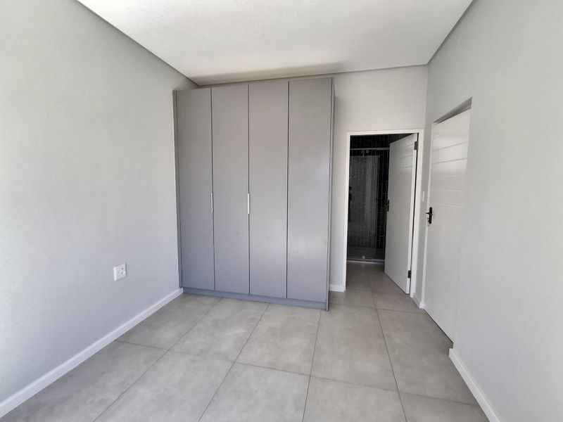 A clean, modern bedroom featuring neutral grey tiled flooring, built-in wardrobes, and direct access to an en-suite bathroom.