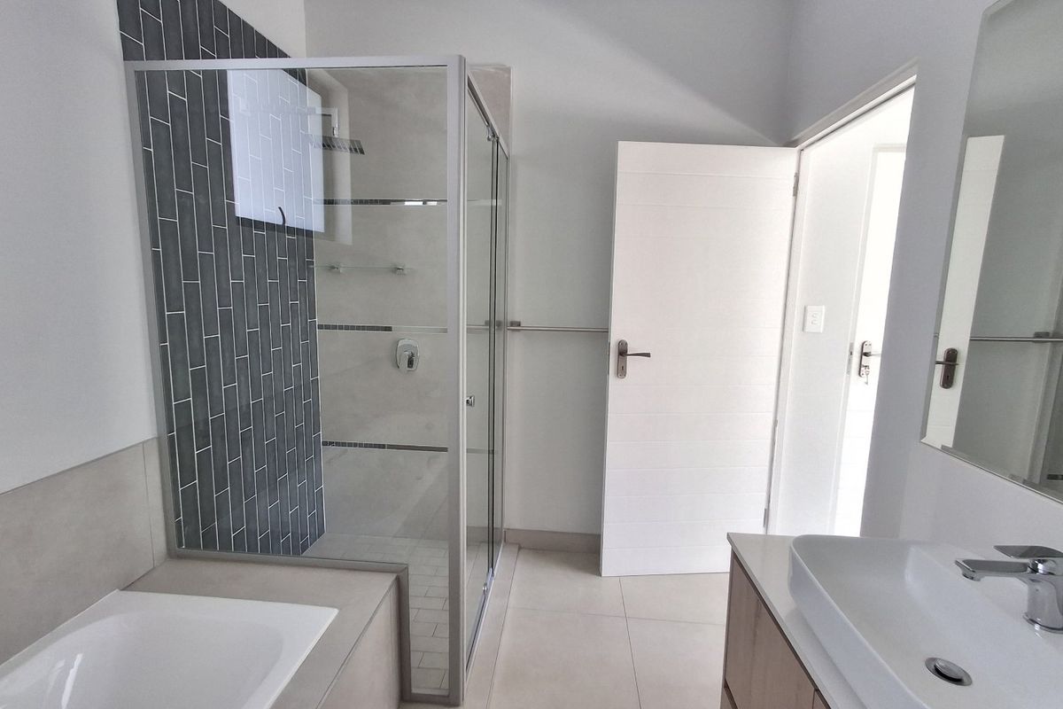 Modern bathroom featuring a glass-enclosed shower, built-in bathtub, and a sleek vanity with a vessel sink, finished with contemporary tiling.