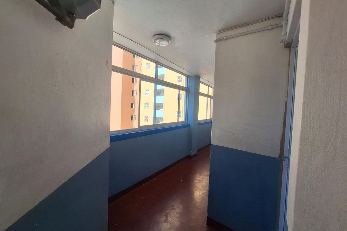 A functional apartment hallway featuring sliding windows, painted walls with a blue dado, and exposed conduit, presenting a basic and dated aesthetic.