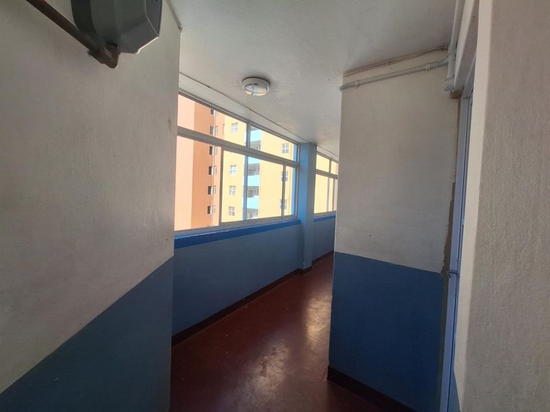 A functional apartment hallway featuring sliding windows, painted walls with a blue dado, and exposed conduit, presenting a basic and dated aesthetic.
