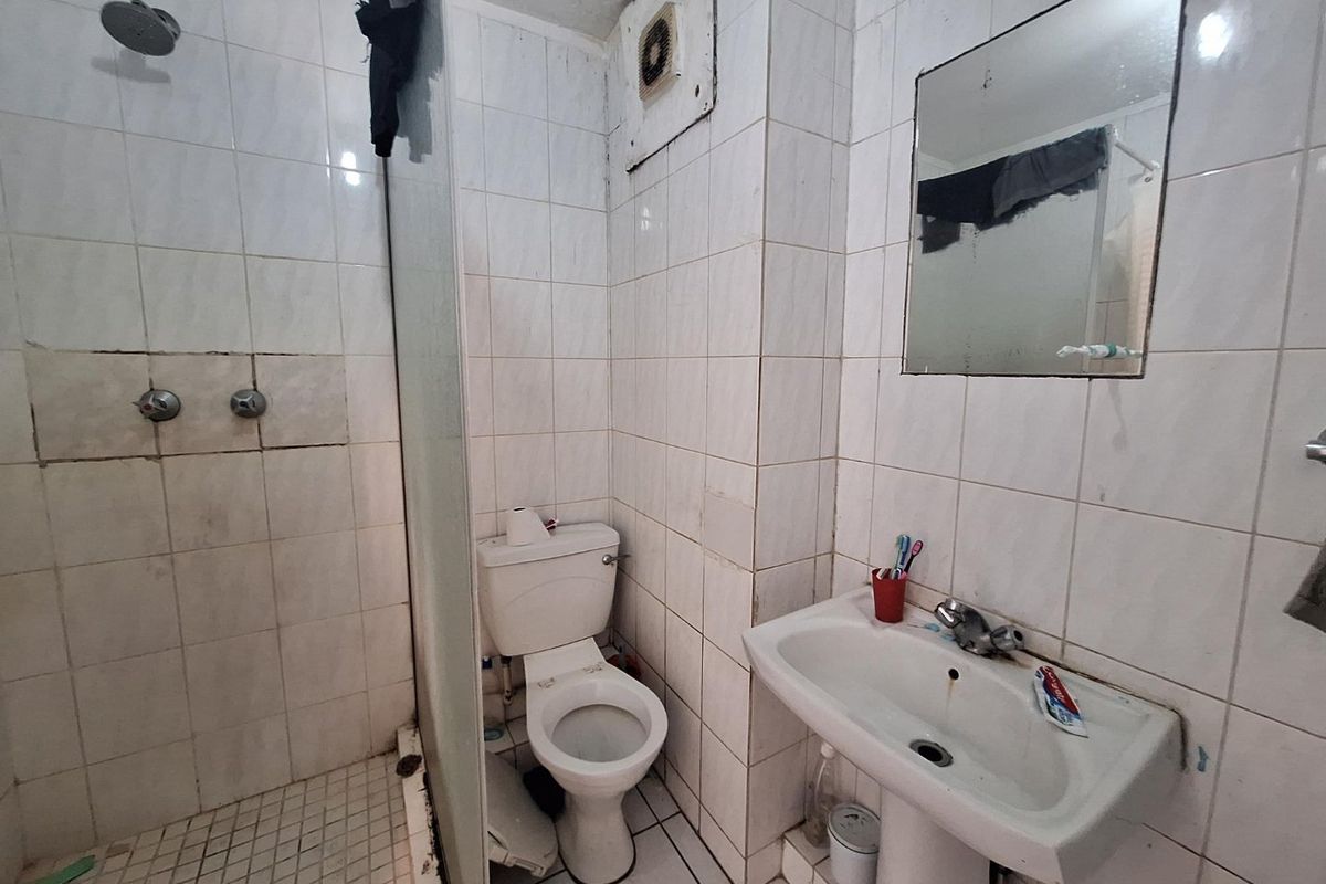 Compact bathroom featuring a shower, pedestal basin, and toilet with full-height wall tiling. The space would benefit from modernization and cosmetic updates.