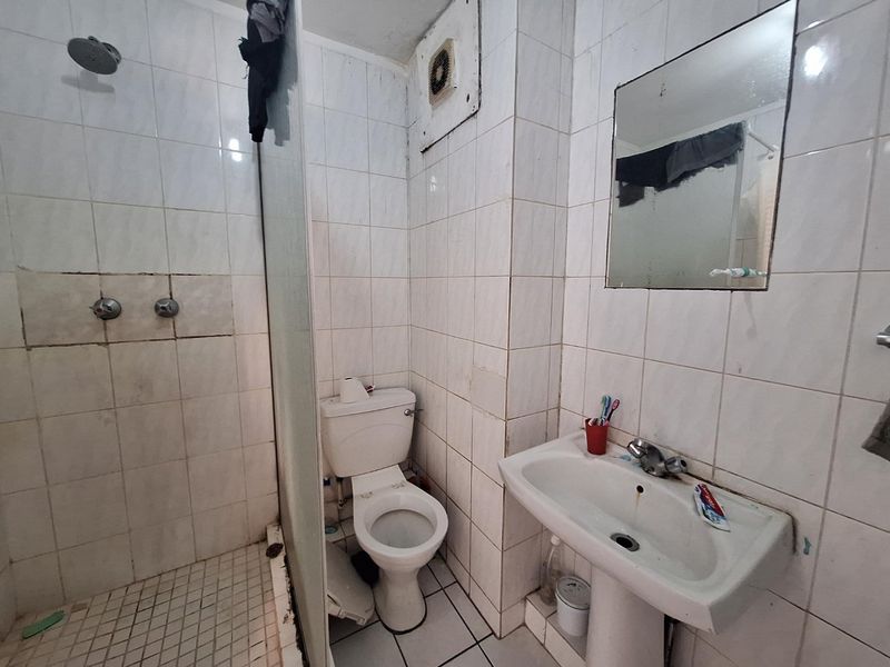 Compact bathroom featuring a shower, pedestal basin, and toilet with full-height wall tiling. The space would benefit from modernization and cosmetic updates.