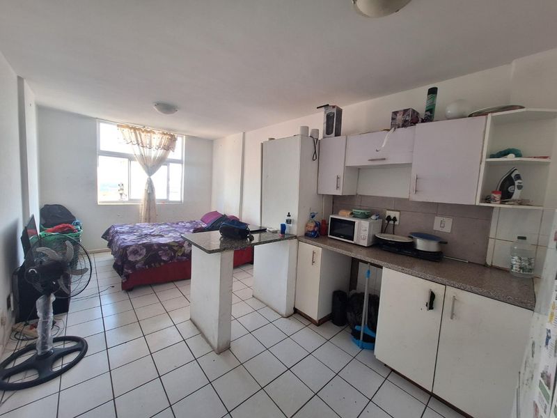 Open-plan studio apartment featuring a compact kitchen with granite countertops, built-in cabinetry, and tiled flooring throughout.
