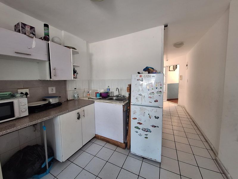A compact kitchen featuring tiled flooring, laminate countertops, and a stainless steel sink, offering a functional layout in need of cosmetic updates.