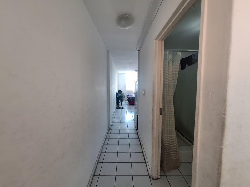 A narrow hallway with tiled flooring leading towards a bedroom, with a bathroom entrance visible on the right side.