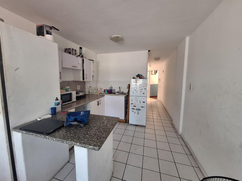 A functional kitchen area featuring granite countertops, built-in cabinetry, a stainless steel sink, and tiled flooring, leading into a narrow hallway.
