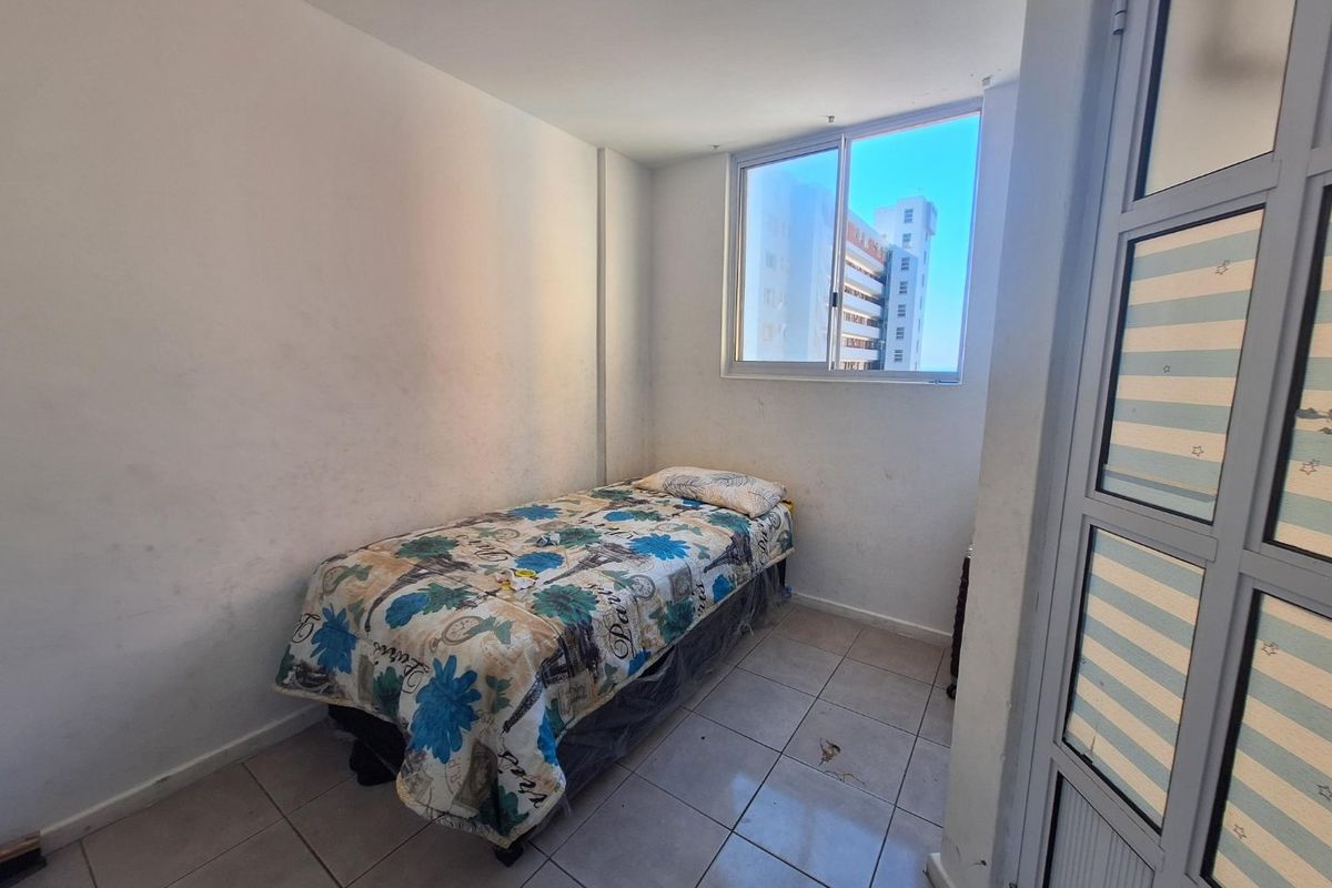A compact bedroom featuring tiled flooring and an aluminium-framed window, requiring cosmetic updates to the wall finishes and flooring.