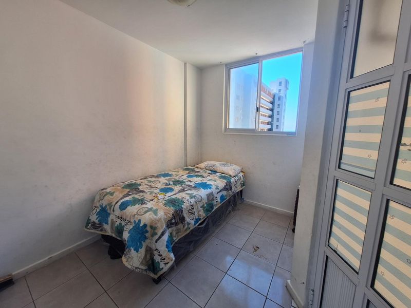 A compact bedroom featuring tiled flooring and an aluminium-framed window, requiring cosmetic updates to the wall finishes and flooring.
