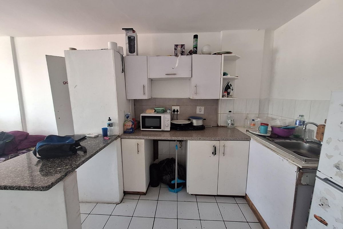 A compact kitchen featuring white cabinetry, granite countertops, and tiled flooring, offering a functional layout in need of cosmetic updates.