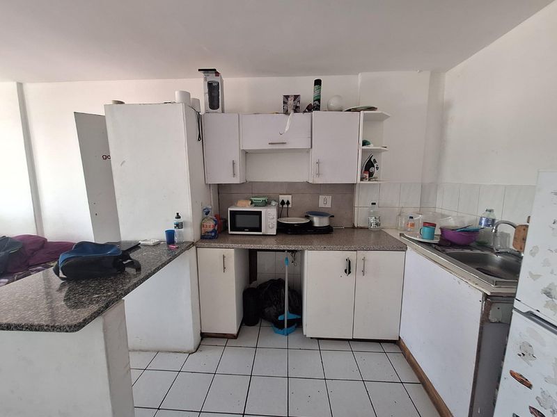 A compact kitchen featuring white cabinetry, granite countertops, and tiled flooring, offering a functional layout in need of cosmetic updates.