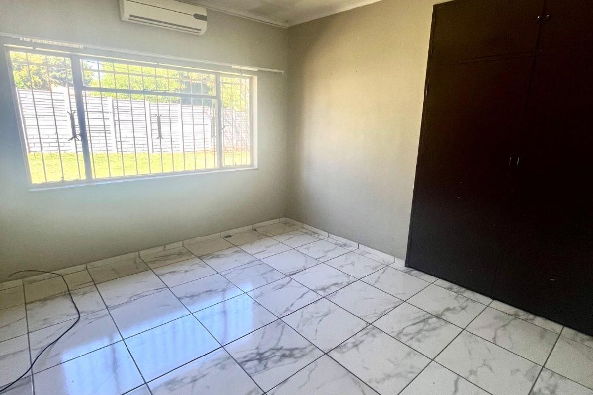 A bright, empty bedroom featuring modern marble-look tiled flooring, built-in cupboards, a ceiling fan, and an air conditioning unit.