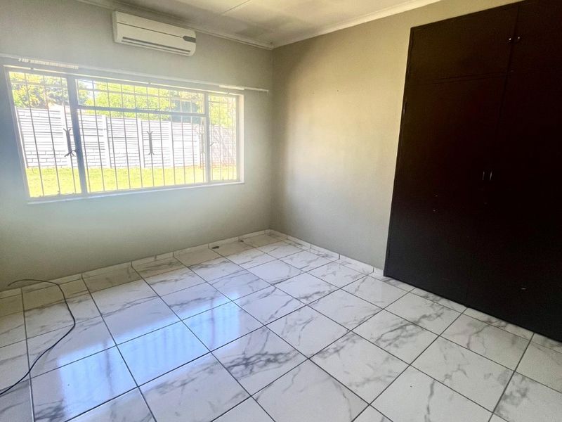 A bright, empty bedroom featuring modern marble-look tiled flooring, built-in cupboards, a ceiling fan, and an air conditioning unit.