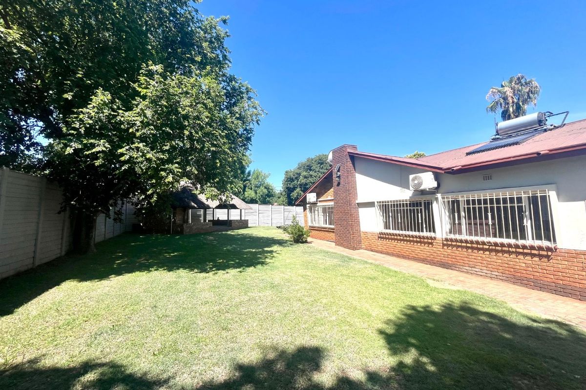 Spacious rear garden featuring a lawn, brick-accented exterior wall, security bars, solar water heating system, and a detached thatched lapa area.