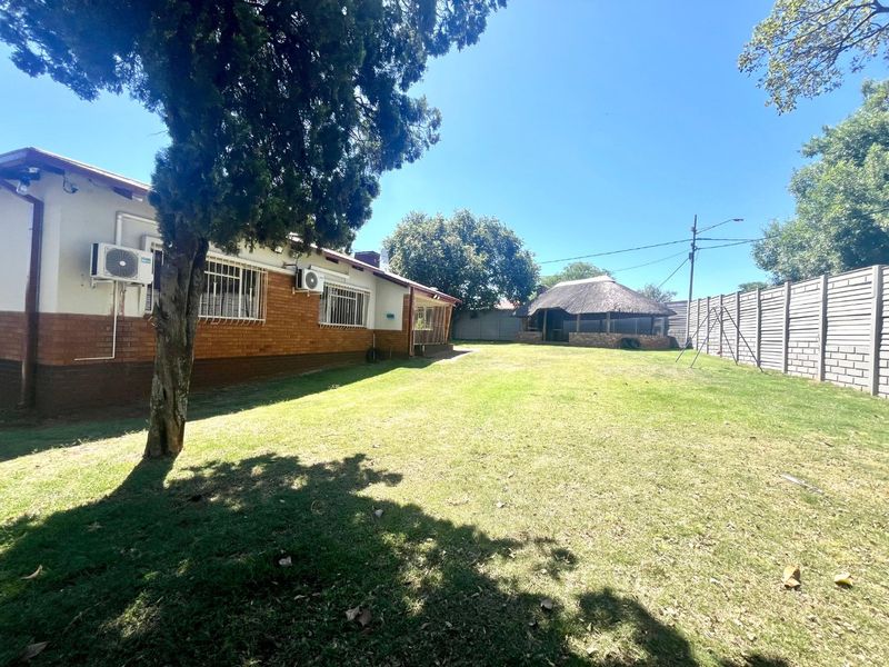 Spacious rear garden featuring a brick-clad house exterior, a traditional thatched lapa, and secure perimeter fencing.