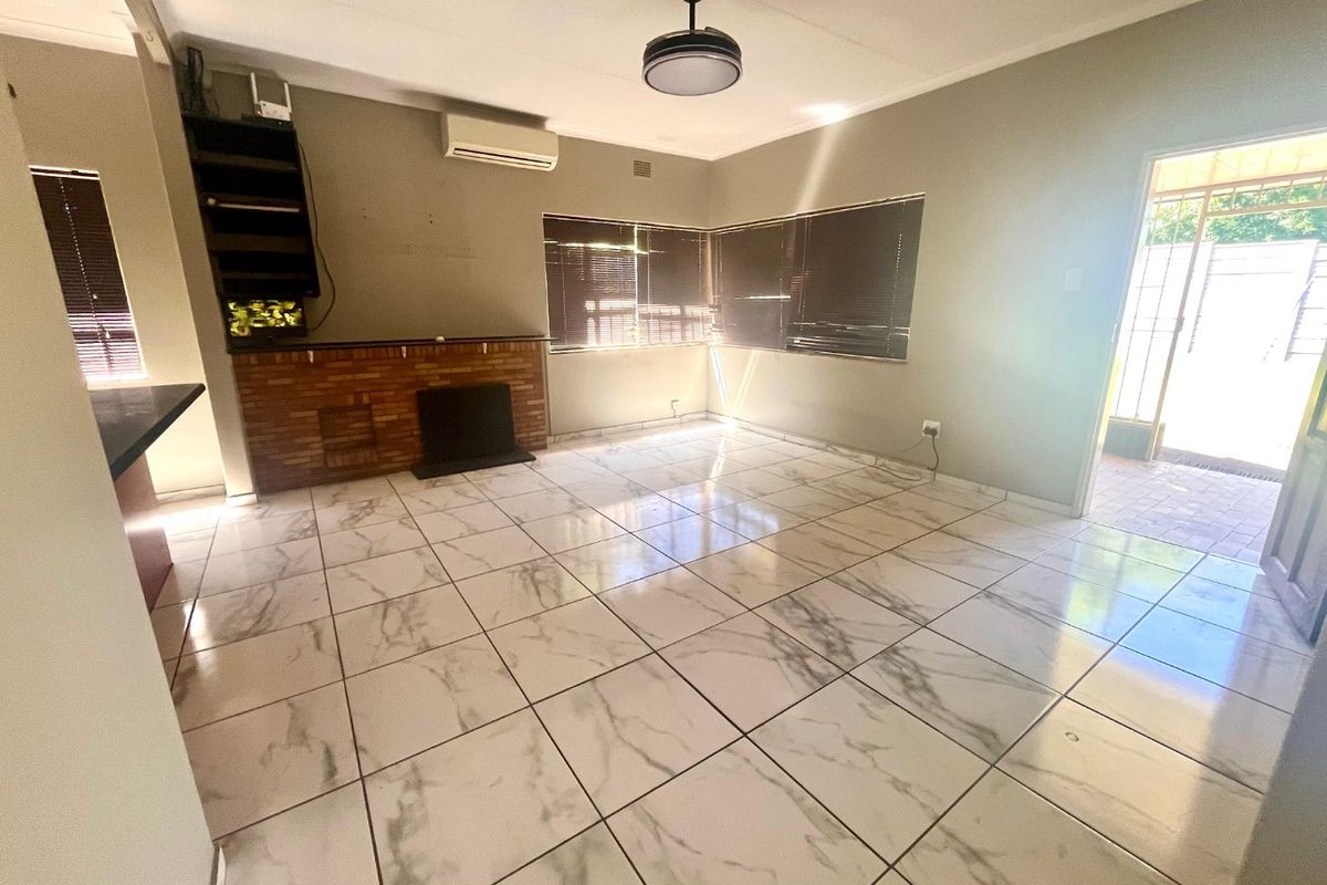 Spacious living room featuring marble-look floor tiles, a brick fireplace, and a wall-mounted air conditioning unit.