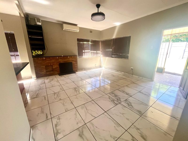 Spacious living room featuring marble-look floor tiles, a brick fireplace, and a wall-mounted air conditioning unit.