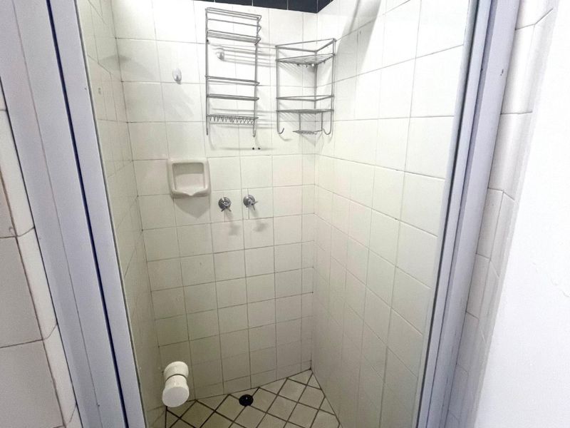 A compact shower stall featuring white wall tiles with a black border, a rain shower head, and a tiled floor.