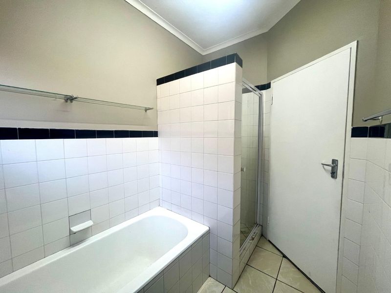 A functional bathroom featuring a built-in bathtub, a separate shower enclosure, and neutral tiled finishes throughout.