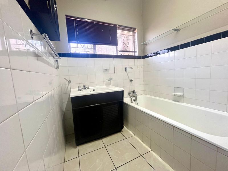 A functional bathroom featuring a built-in vanity, bathtub, and classic white wall tiling with a dark accent border.