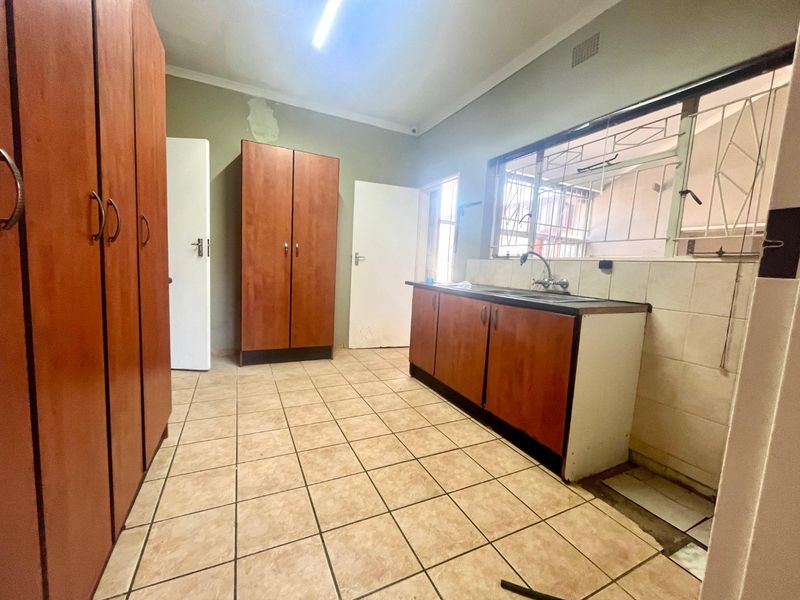 A functional scullery or utility area featuring built-in wooden cabinetry, a stainless steel sink, and tiled flooring, requiring some cosmetic maintenance.