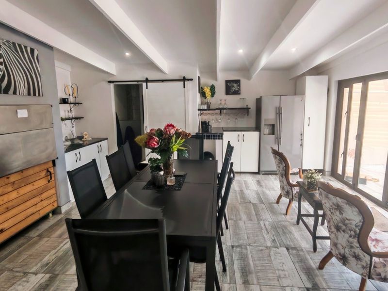 Spacious open-plan living and dining area featuring exposed ceiling beams, tiled flooring, a built-in braai, and direct access to the outdoor patio.