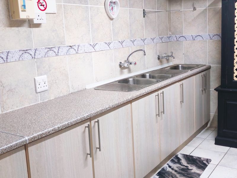 A functional scullery area featuring laminate cabinetry, a durable laminate countertop, and a double stainless steel sink with wall-mounted fixtures.