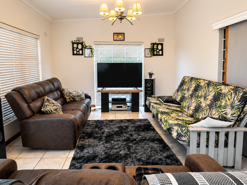 A comfortable living room featuring tiled flooring, venetian blinds, and a sliding door, providing a functional and well-lit space for relaxation.