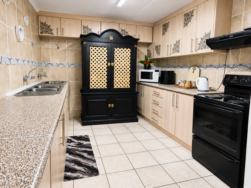 A functional kitchen featuring light wood-tone cabinetry, granite-look countertops, ceramic tiling, and a freestanding electric stove with an integrated extractor fan.