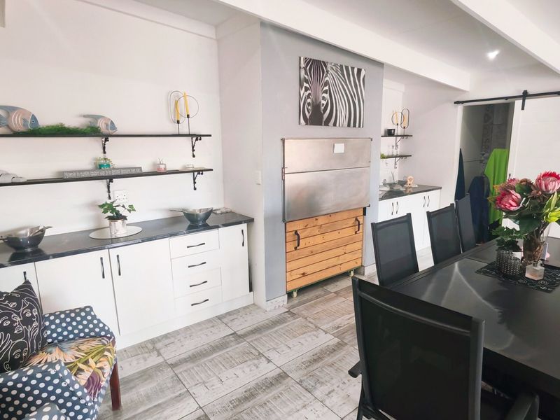 Open plan dining and kitchen area featuring modern white cabinetry, stone countertops, built-in braai, and stylish tiled flooring with a sliding barn door.