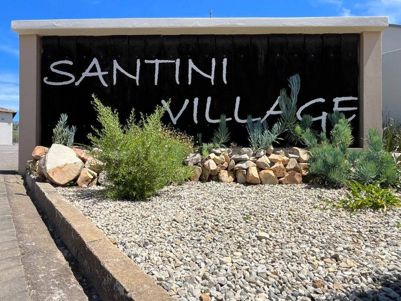 The entrance signage for Santini Village, featuring a landscaped garden bed with stone accents and gravel ground cover.