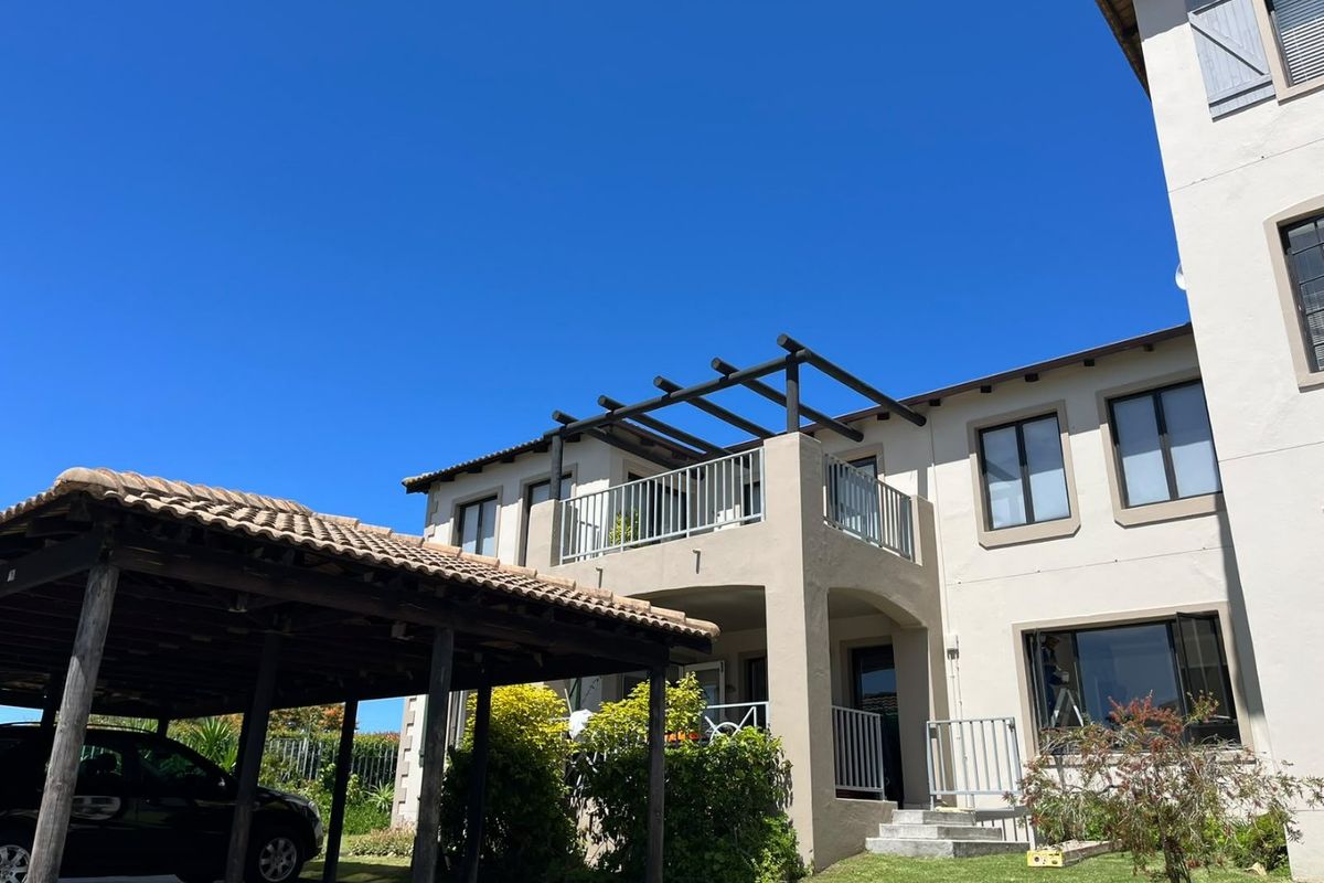 Front elevation of the apartment building featuring a covered carport, a balcony with a timber pergola, and well-maintained stucco exterior finishes.