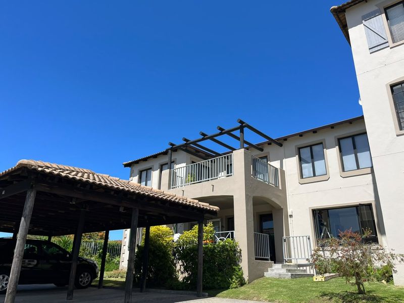 Front elevation of the apartment building featuring a covered carport, a balcony with a timber pergola, and well-maintained stucco exterior finishes.
