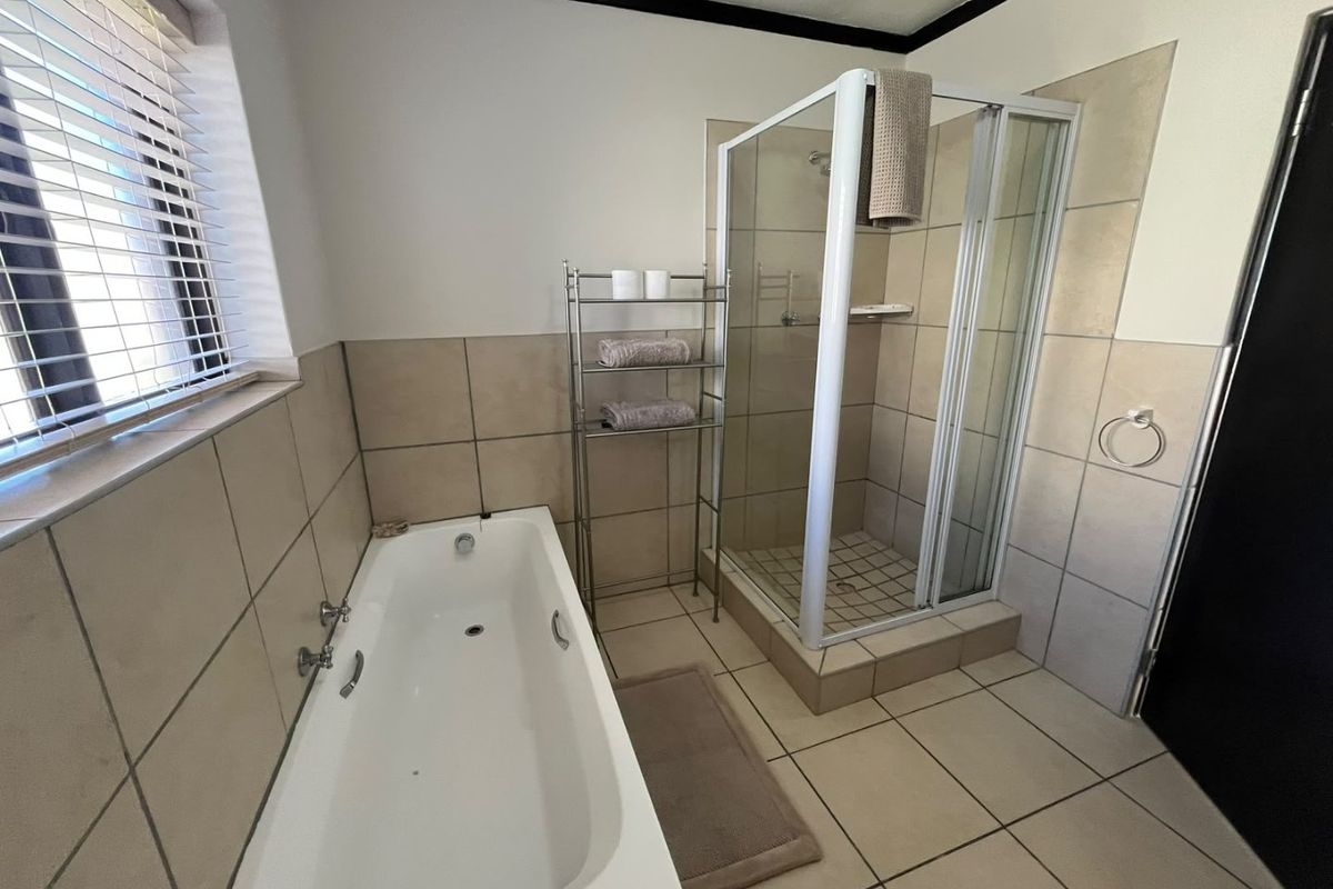 A functional bathroom featuring a built-in bathtub, a separate glass-enclosed shower, and neutral floor-to-wall tiling.