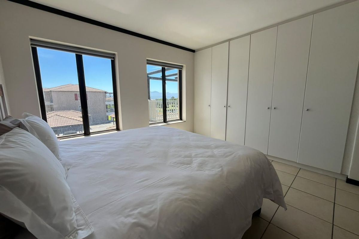 A bright bedroom featuring built-in cupboards, tiled flooring, and large windows offering natural light and exterior views.