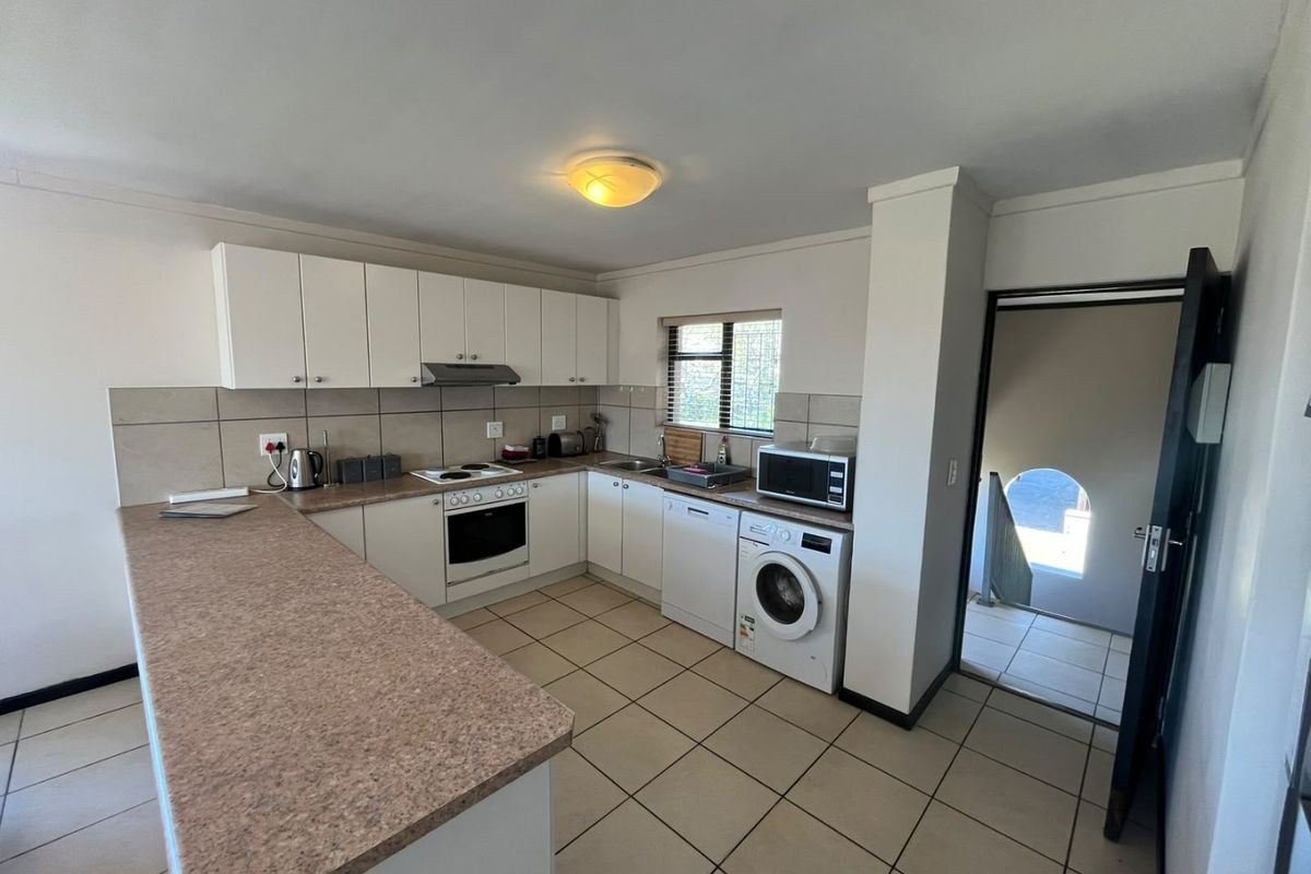 Functional kitchen featuring white cabinetry, laminate countertops, built-in oven and hob, and tiled flooring with direct access to an adjacent hallway.