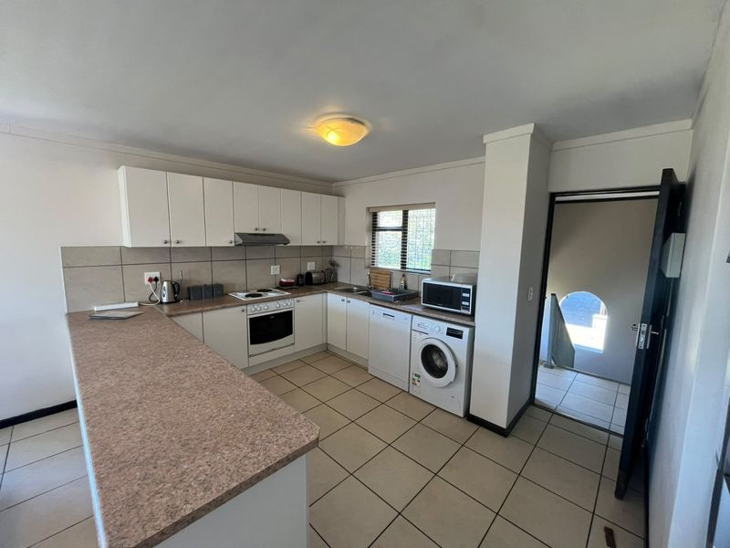 Functional kitchen featuring white cabinetry, laminate countertops, built-in oven and hob, and tiled flooring with direct access to an adjacent hallway.
