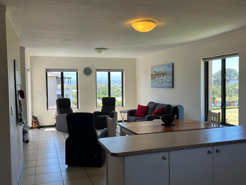 An open-plan living and dining area featuring tiled flooring, neutral walls, and large windows providing natural light and scenic views.