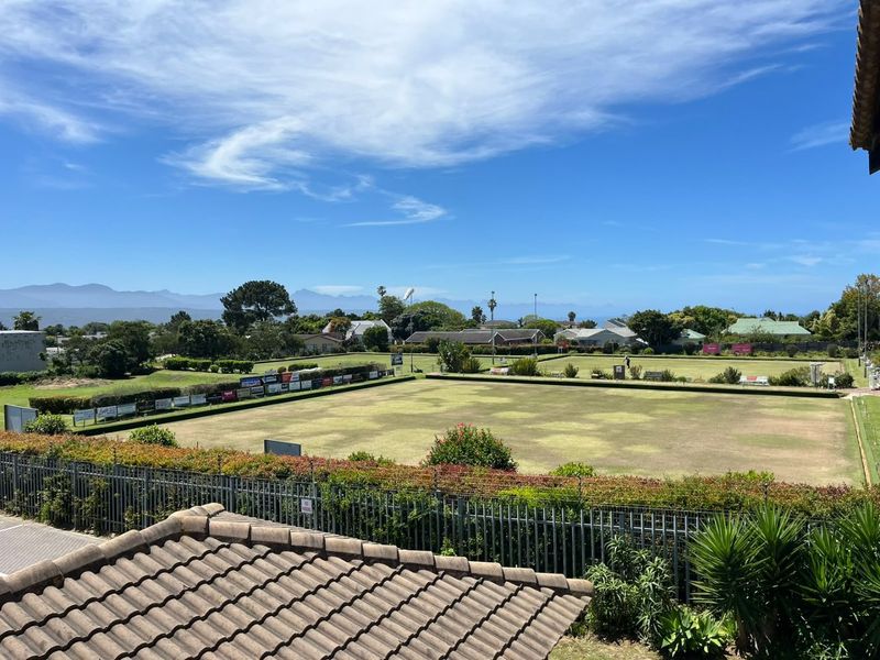 Elevated view overlooking a local bowling green and surrounding residential neighborhood with distant mountain scenery.