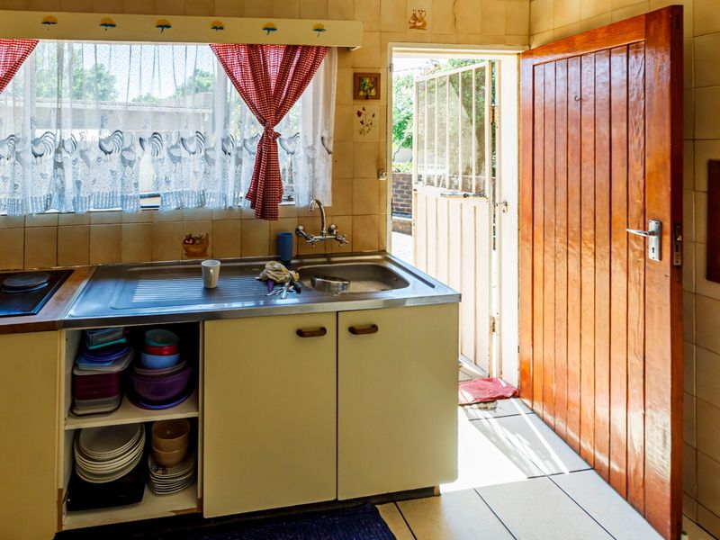 A functional kitchen featuring built-in cabinetry, a stainless steel sink, and direct access to the exterior through a timber door.