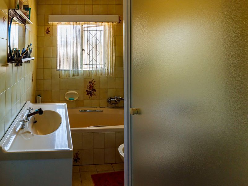 A dated bathroom featuring a built-in vanity, basin, bathtub, and a shower enclosure with frosted glass, finished with traditional wall and floor tiling.