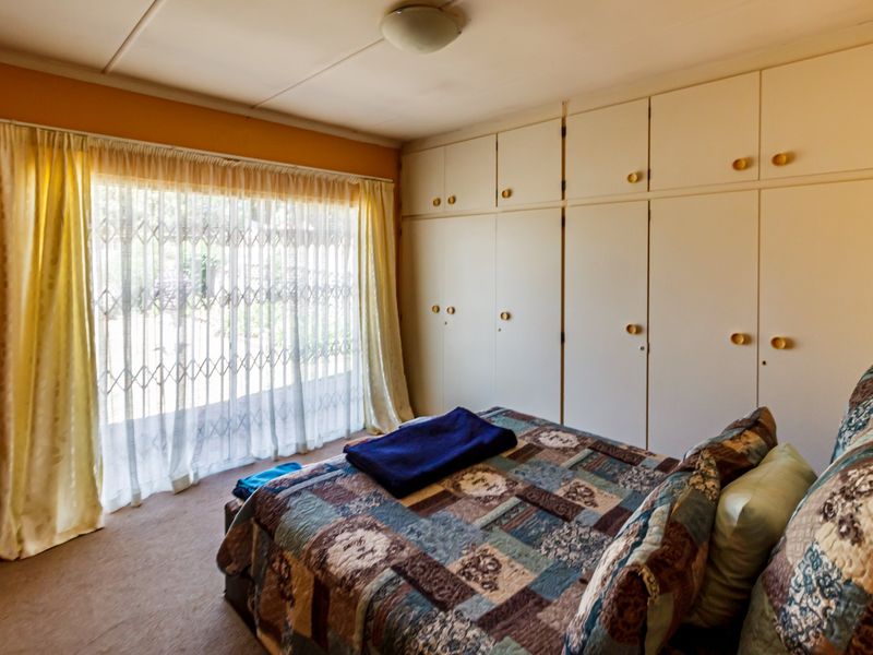 A bedroom featuring extensive built-in cabinetry, a sliding door with a security gate, and neutral carpeting.